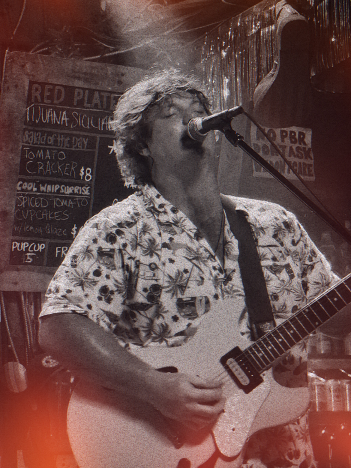 Person singing into microphone while playing guitar in a bar with signs on the wall.