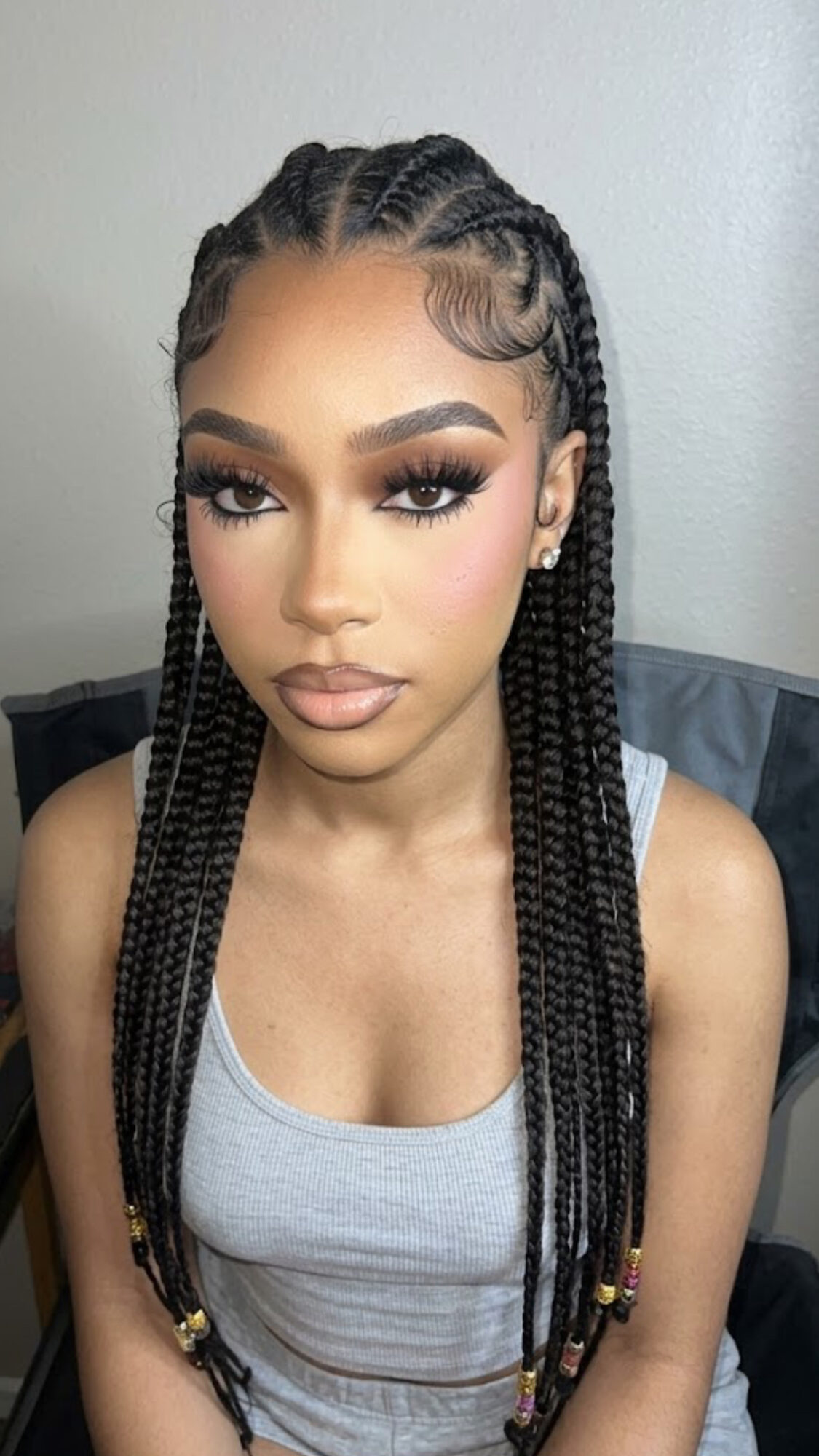 Young woman with braided hairstyle, makeup, and a gray tank top, looking directly at the camera.