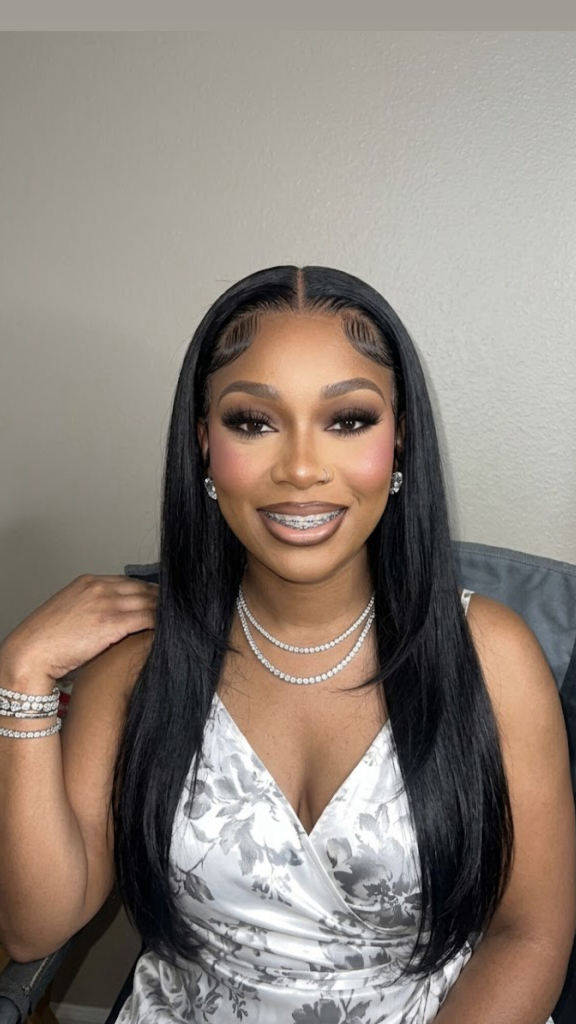 Woman with long black hair, makeup, jewelry, and a floral dress, smiling at the camera.