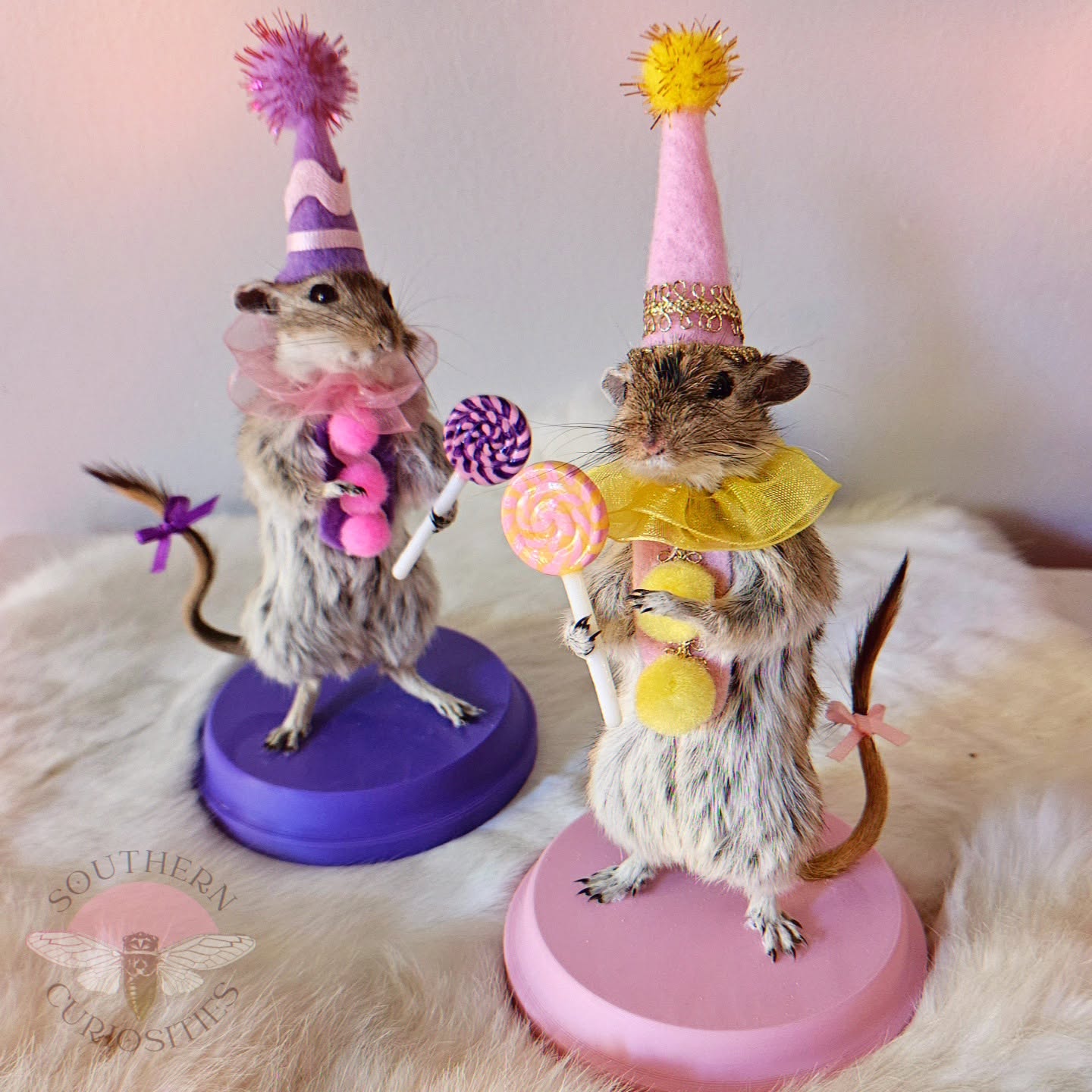 Two decorated mice wearing party hats and costumes, standing on circular bases, on a furry surface.