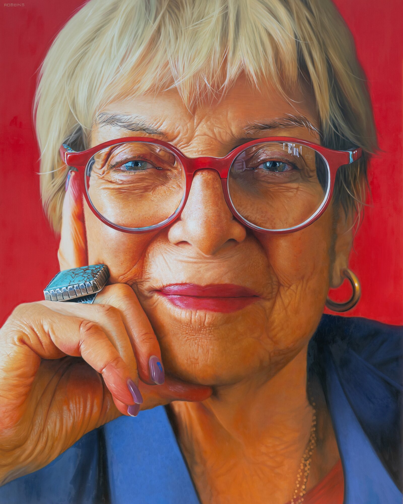 Close-up of an older woman with short blonde hair, red glasses, and a thoughtful expression, resting her chin on her hand.