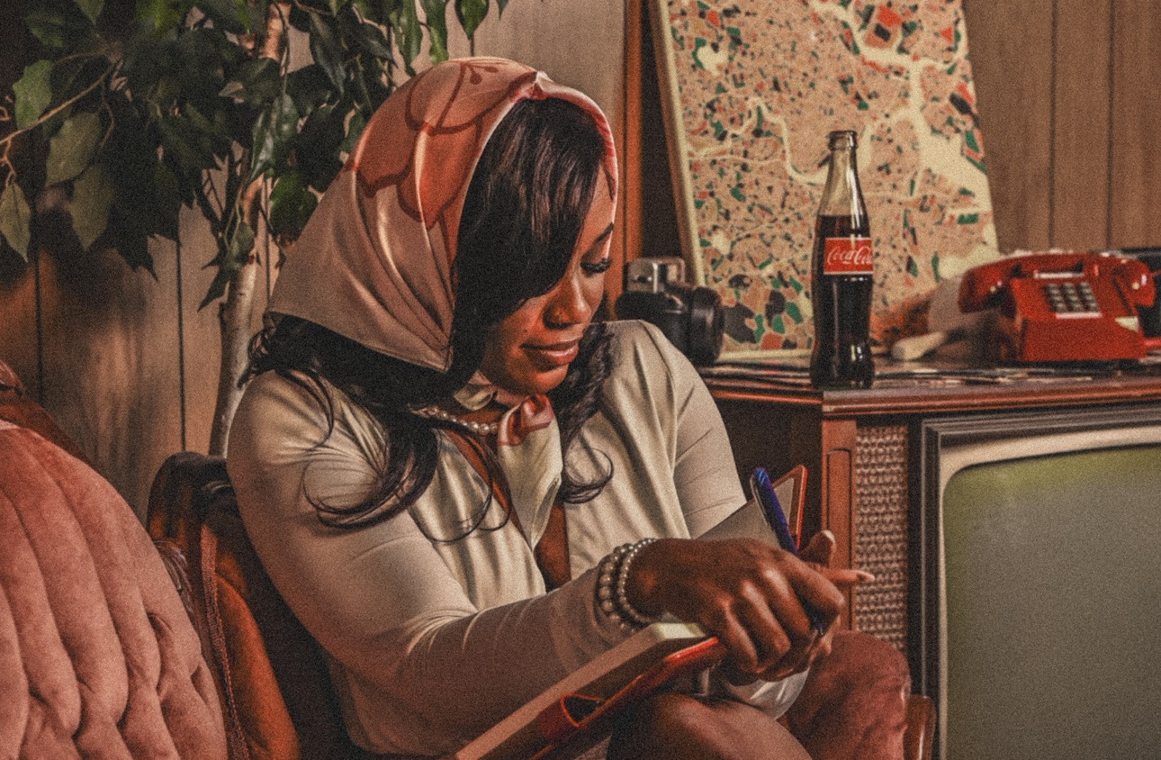 Woman with a headscarf writing in a notebook, sitting in a cozy room with vintage decor.