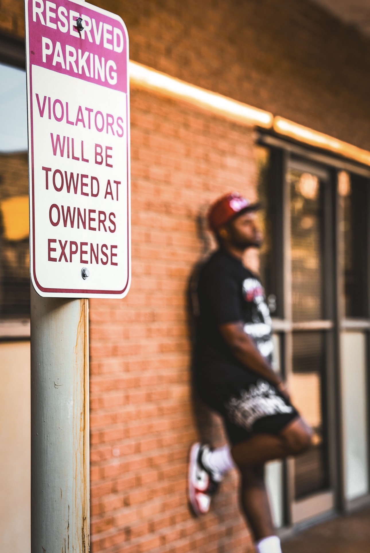 Reserved parking sign with a person standing near a brick building entrance, wearing a cap and dark clothing.