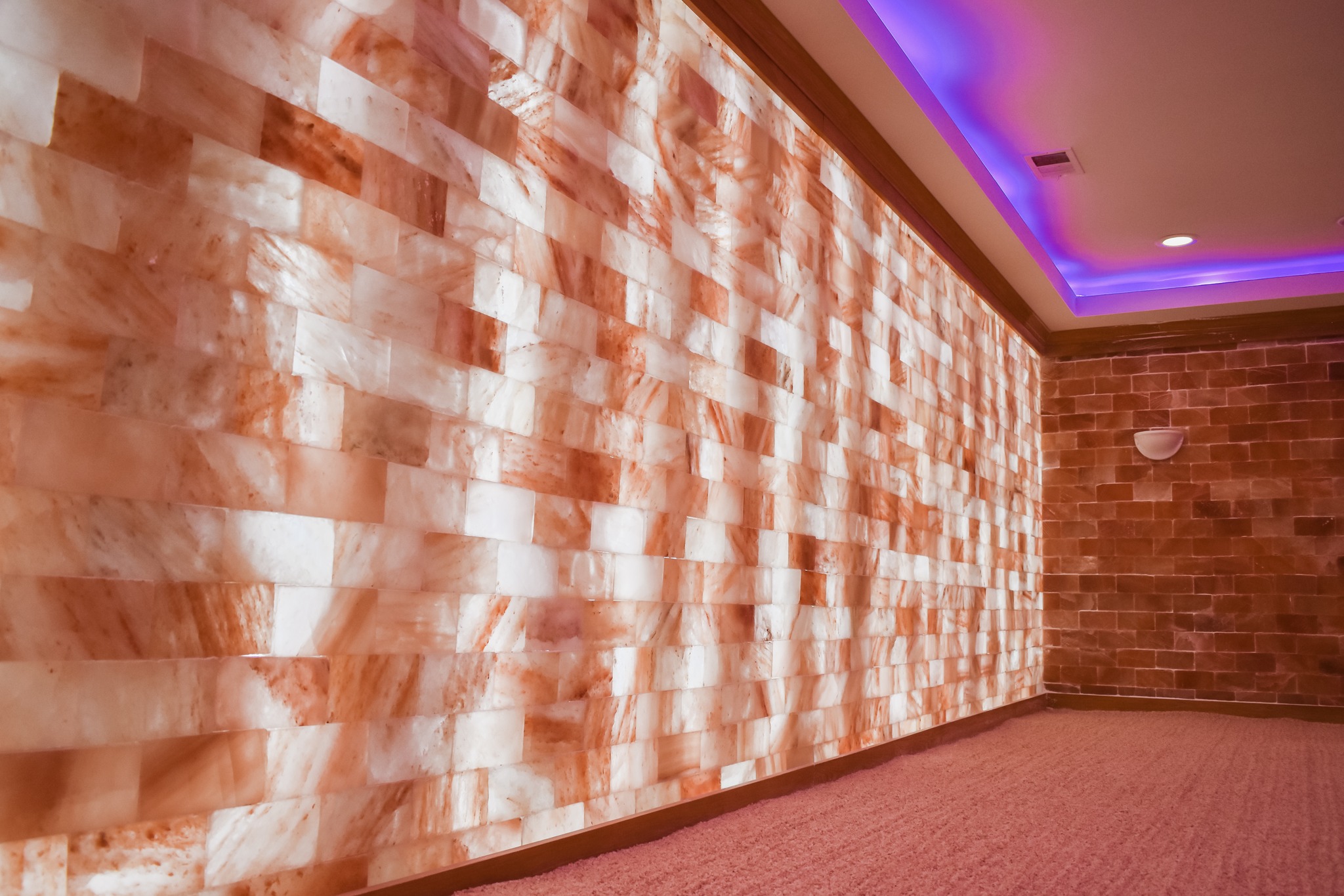 Interior wall with textured, illuminated salt bricks, purple ceiling lighting, and carpeted floor.