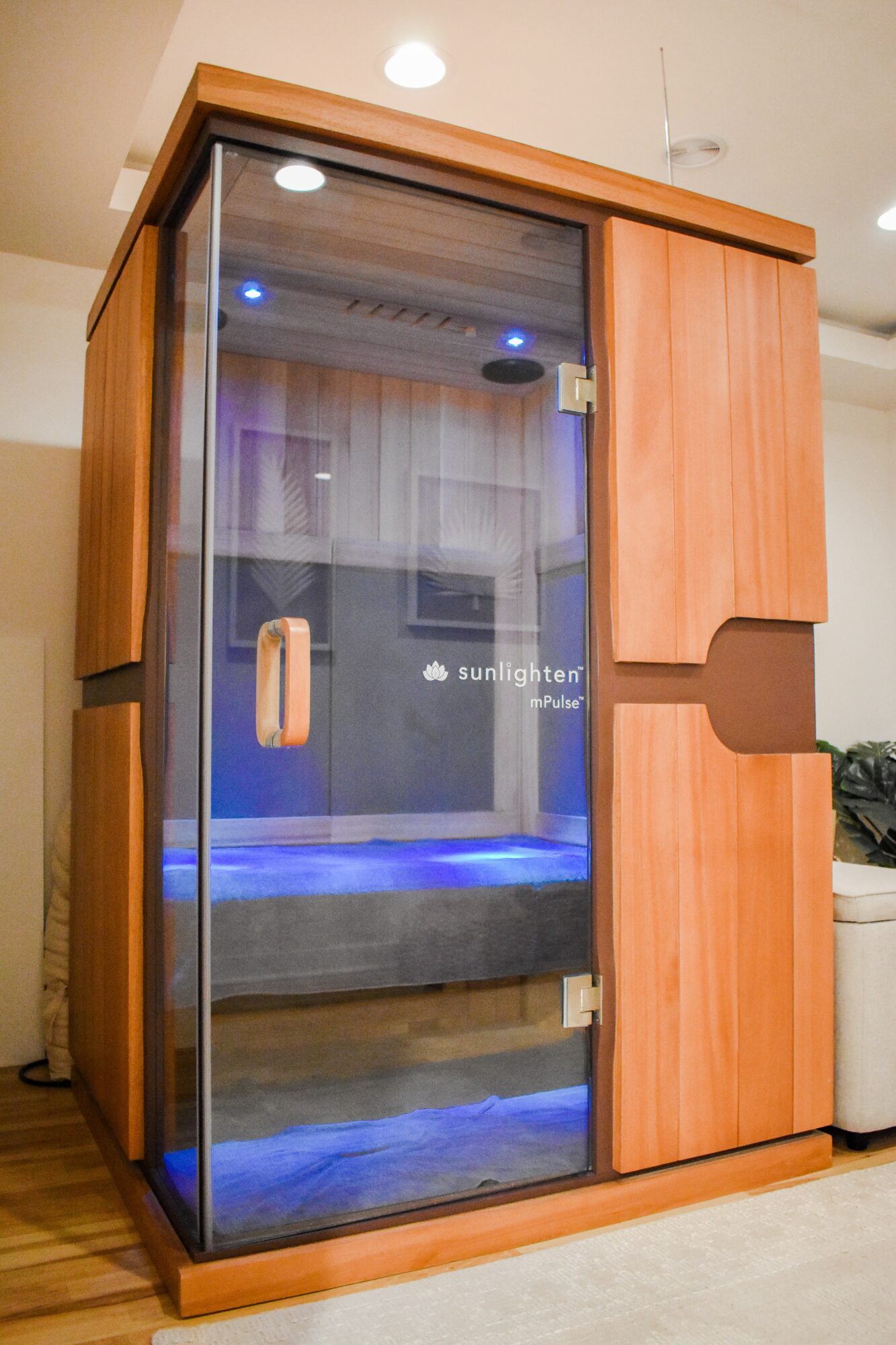 Wooden cabinet with glass door and blue lighting inside, situated in a room with wooden flooring and beige walls.