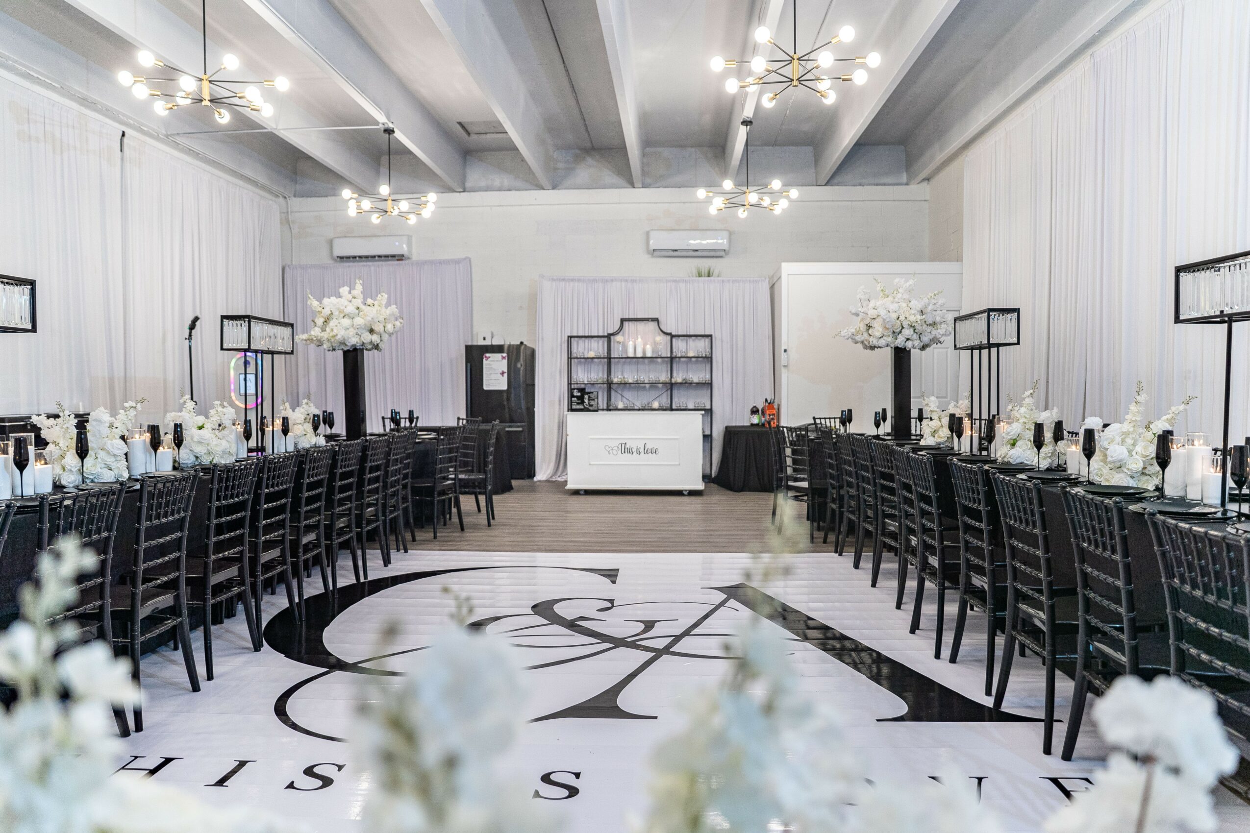 Elegant banquet hall with long tables, white floral centerpieces, and modern lighting fixtures, set for a formal event.