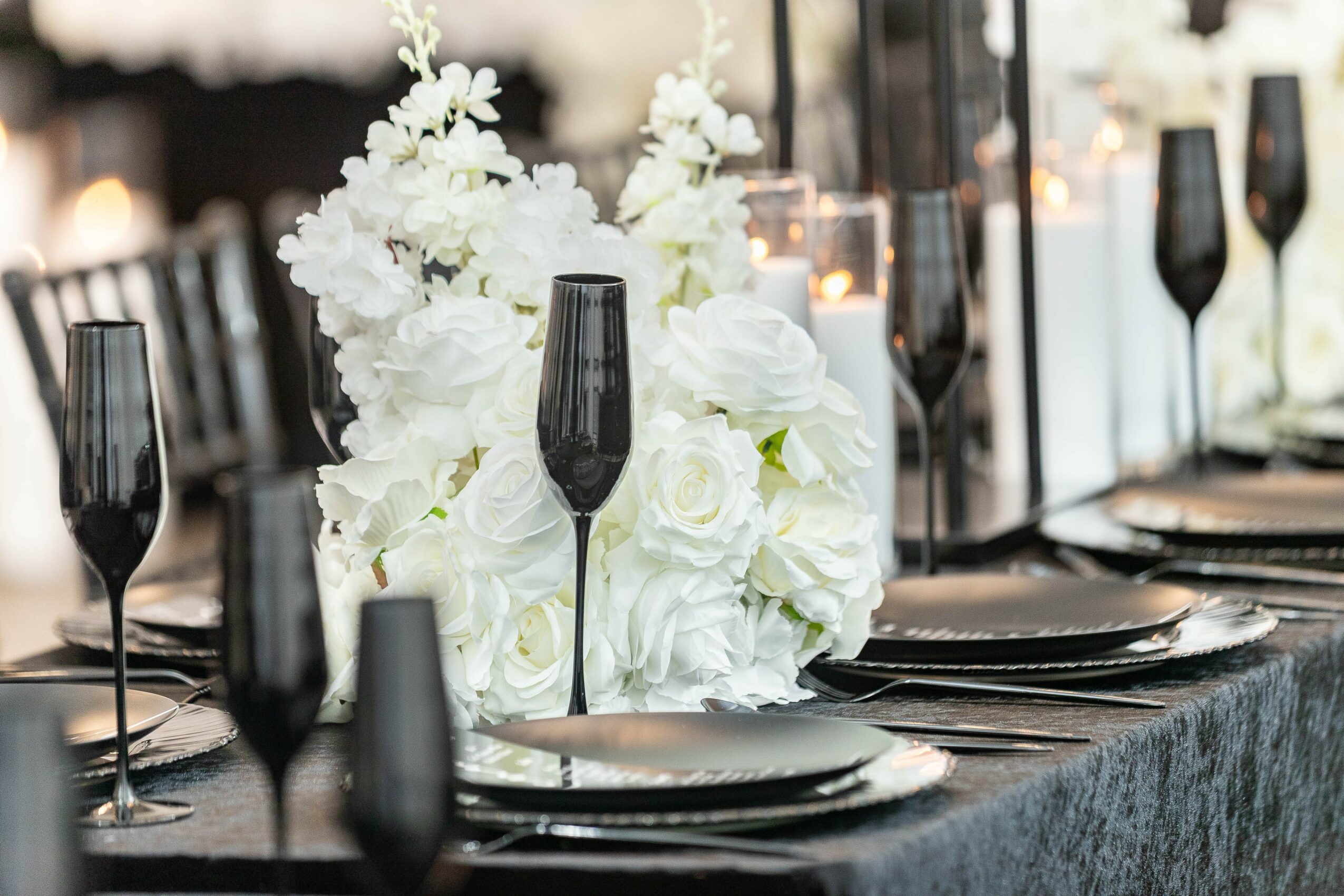 Elegant table setting with black glasses, white floral centerpiece, and black plates on a dark tablecloth.