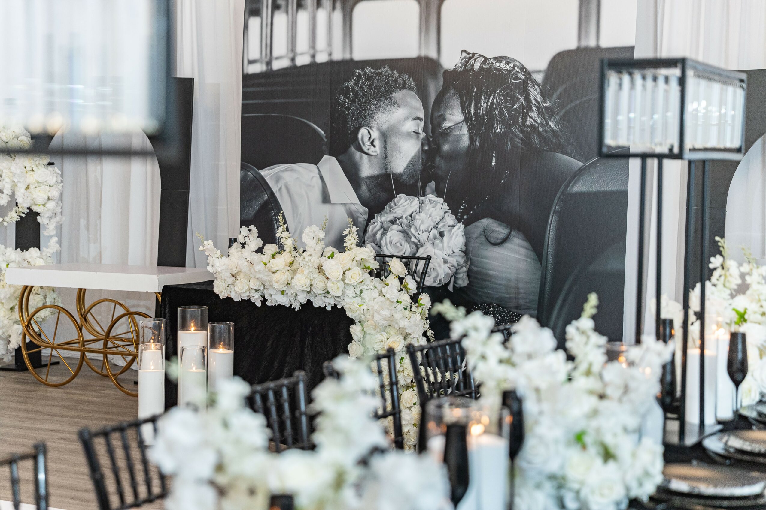 Black and white photo of a couple kissing on a train, with floral decorations and table settings in the foreground.