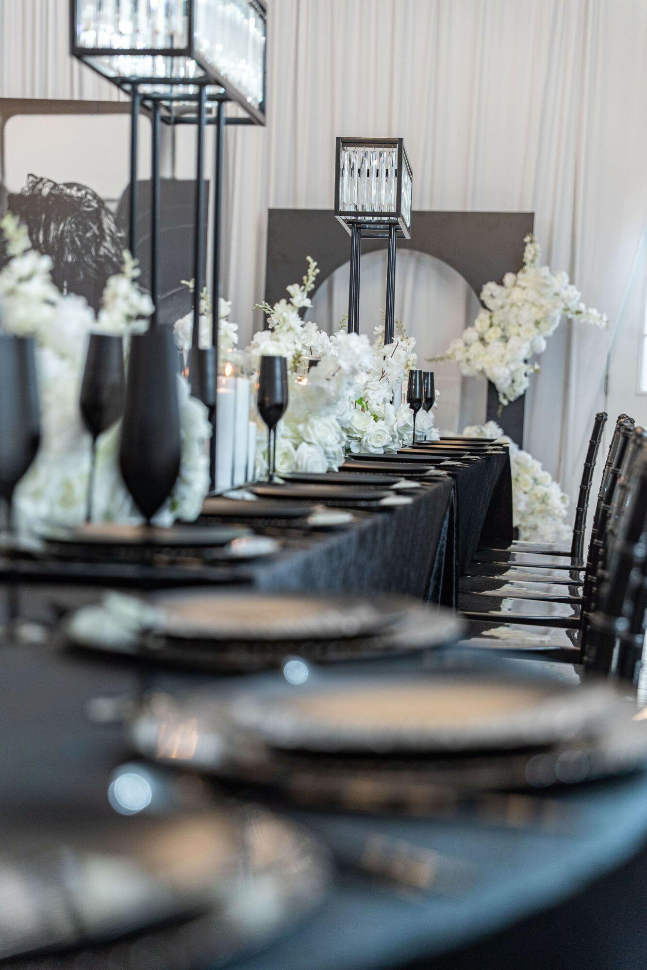 Elegant table setting with black and white floral arrangements, tall candle holders, and a decorative backdrop, in a formal event space.