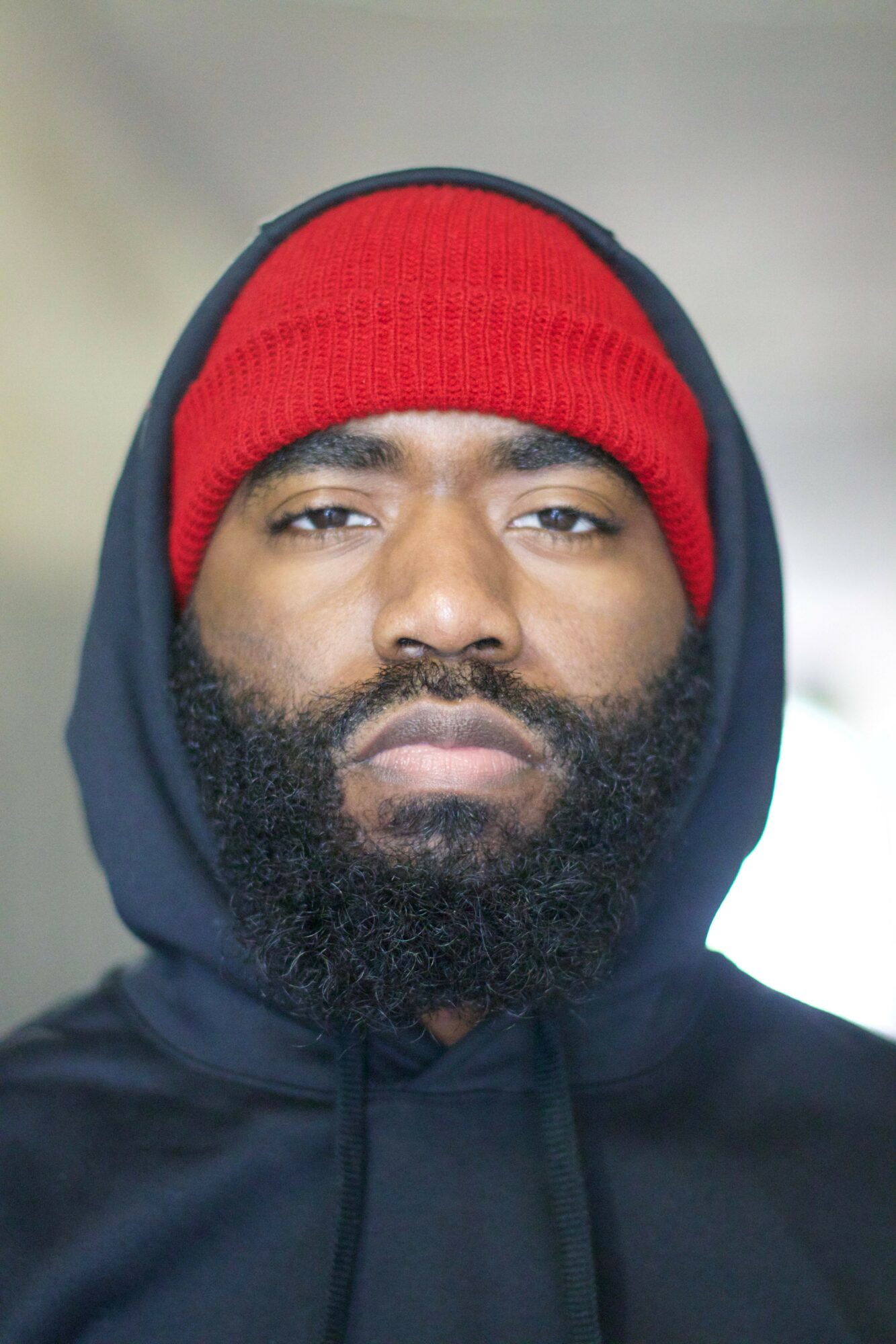 Man with a beard wearing a red beanie and black hoodie, looking at the camera.