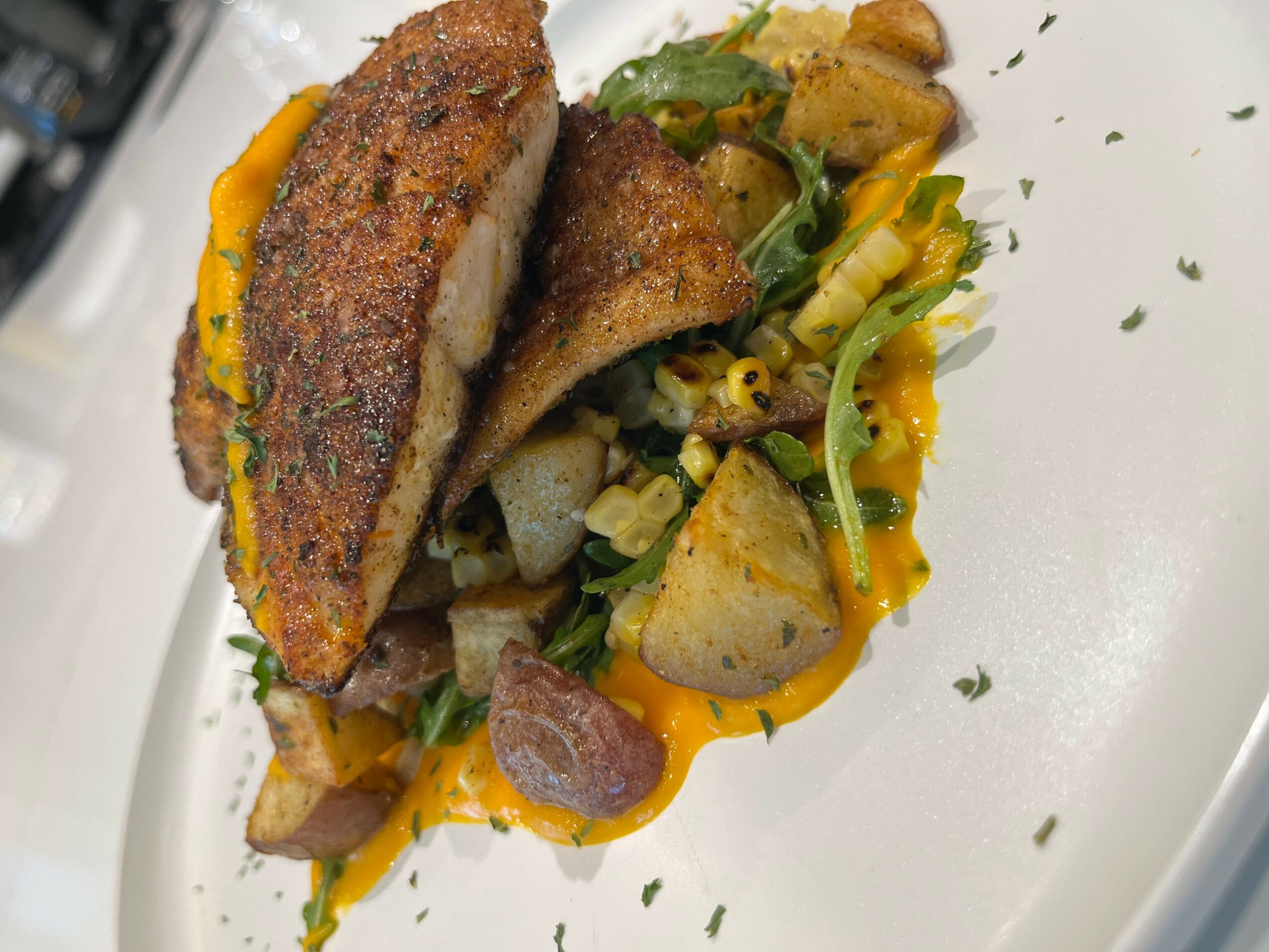 Fried fish fillet with vegetables and sauce on a white plate.