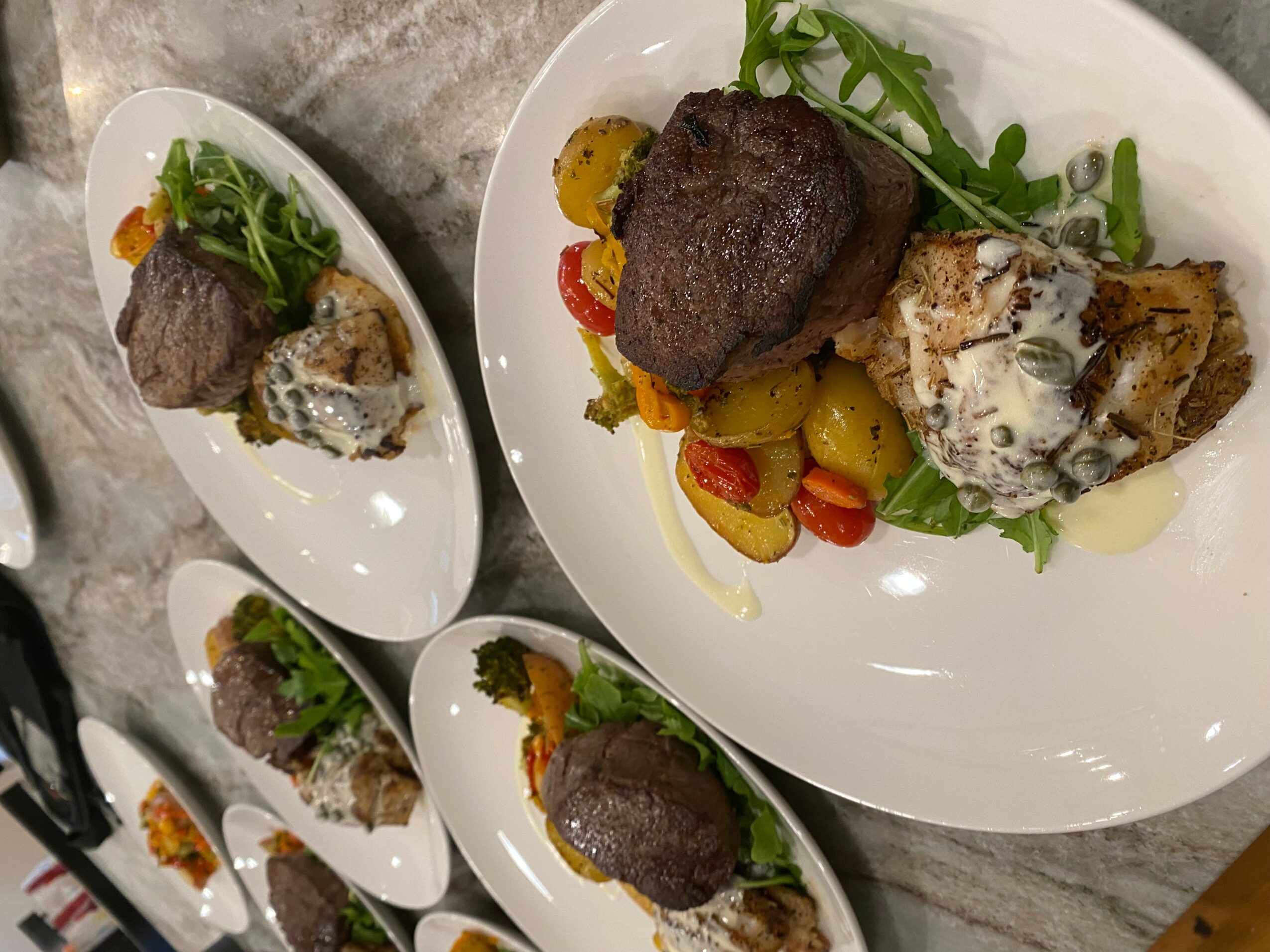 Three plates with cooked meat, vegetables, and garnishes on a gray surface.