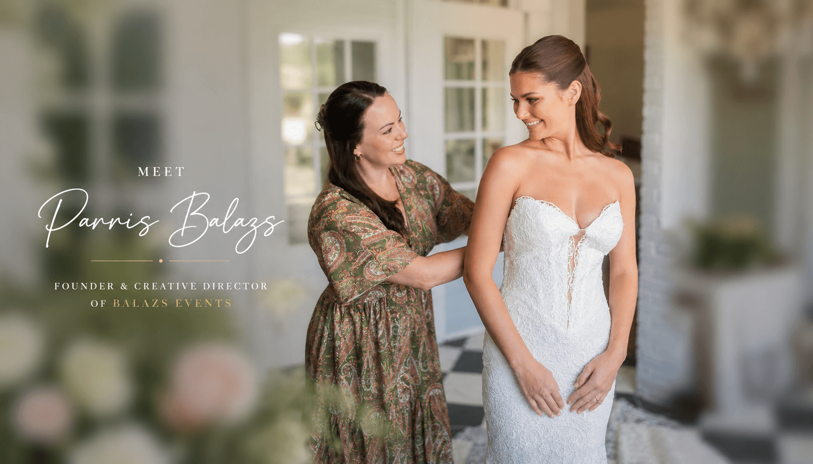 Two women, one in a wedding dress, smiling and holding hands indoors with large windows and plants nearby.