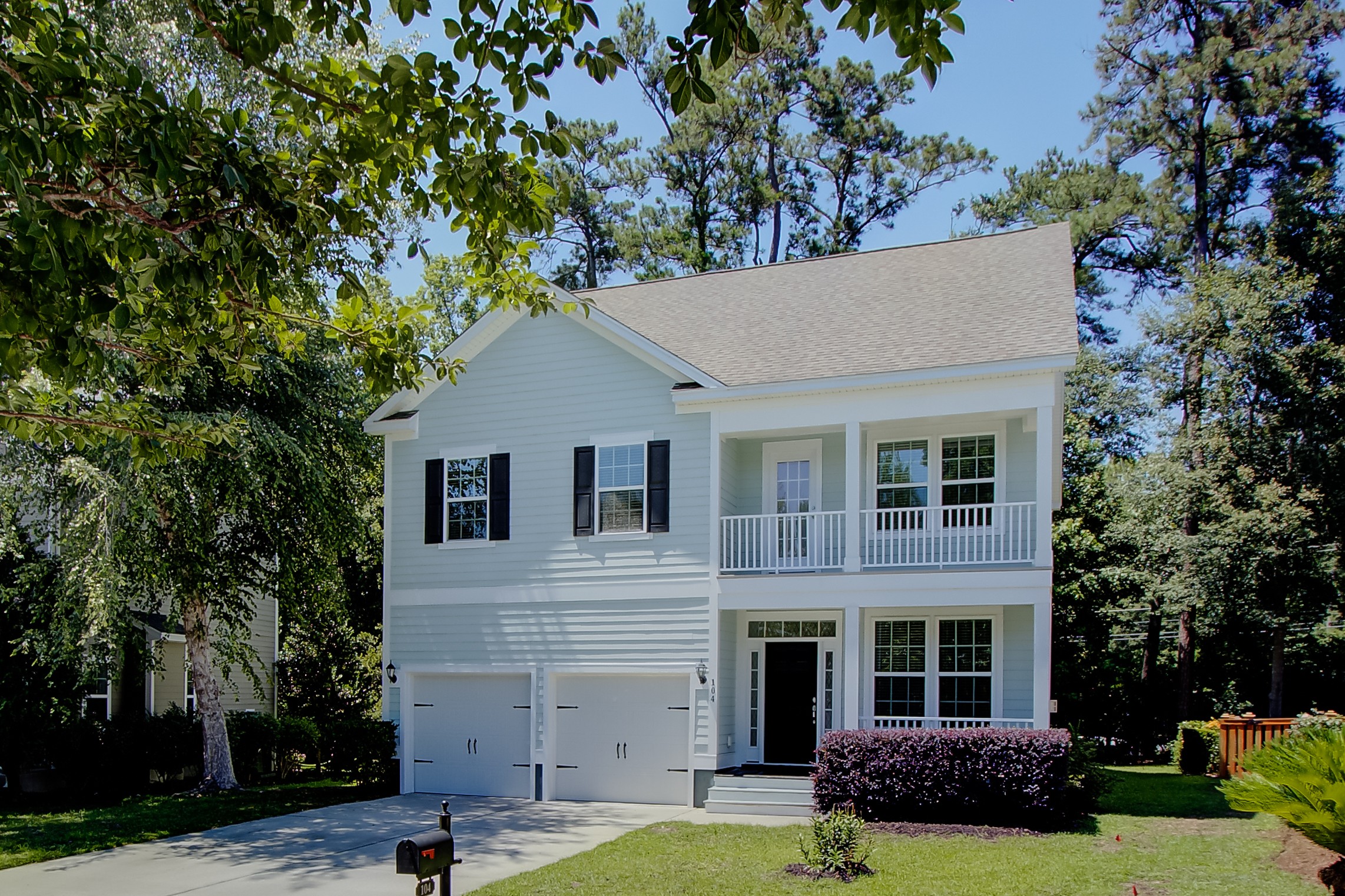 Two-story white house with a garage, front porch, and balcony, surrounded by trees and greenery.
