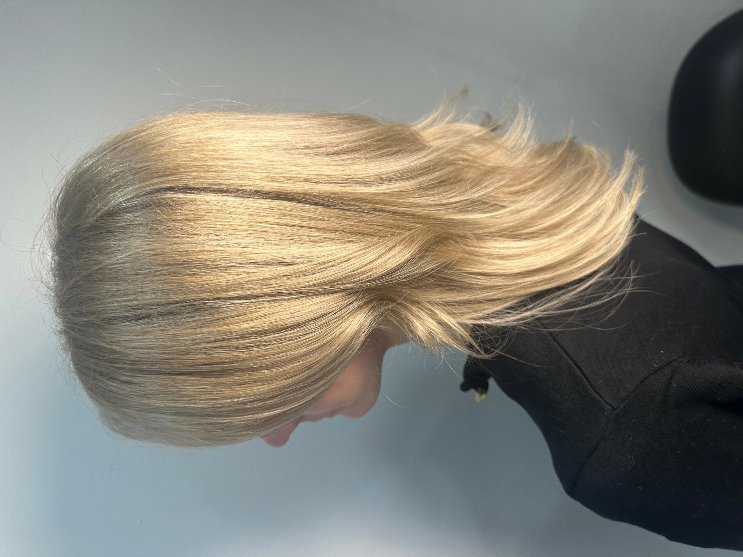 Side view of a person with blonde hair, wearing a black top, against a light background.