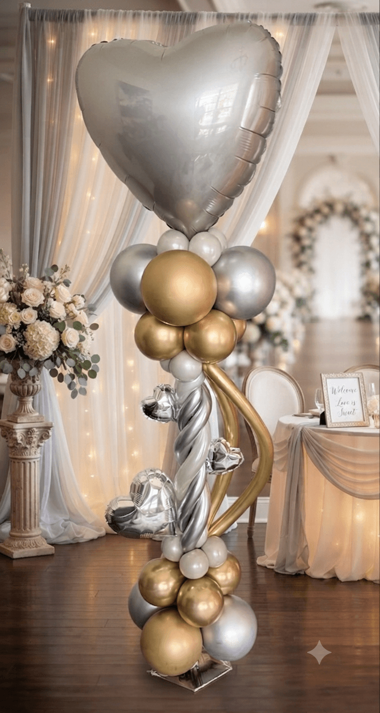 Decorative balloon arrangement with a large silver heart-shaped balloon, smaller gold and silver balloons, and floral decor in a decorated event space.